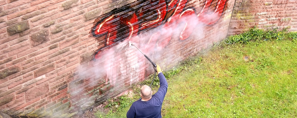 man removing graffiti on a brick wall with power washer